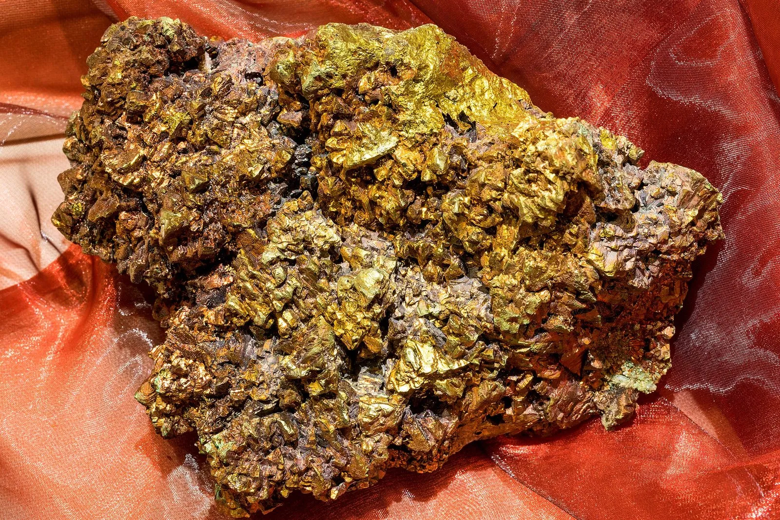Amostra de calcopirita, um minério de cobre, com cristais dourados e acobreados sobre um tecido avermelhado