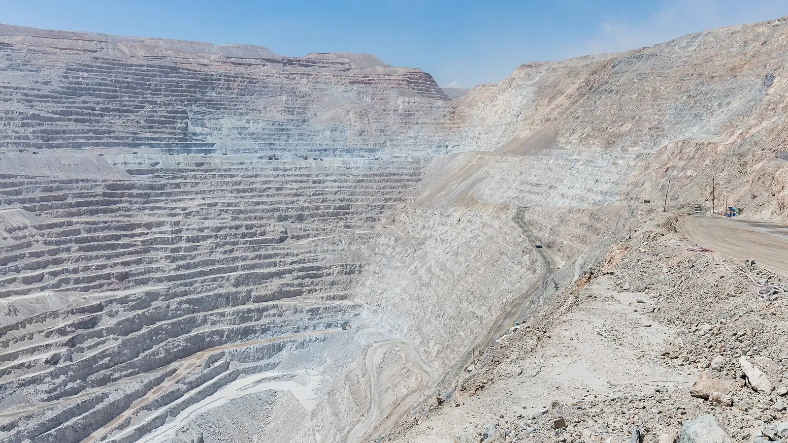Cava de mineração muito grande e profunda, com paredes em degraus de rocha clara, estradas descendo em curva e céu azul ao fundo