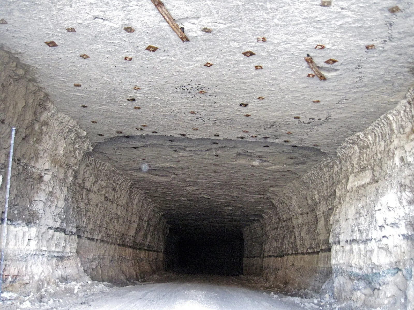 Galeria subterrânea escavada em calcário, com paredes em camadas e o teto cheio de pequenas placas metálicas quadradas, que seguram os tirantes cravados na rocha