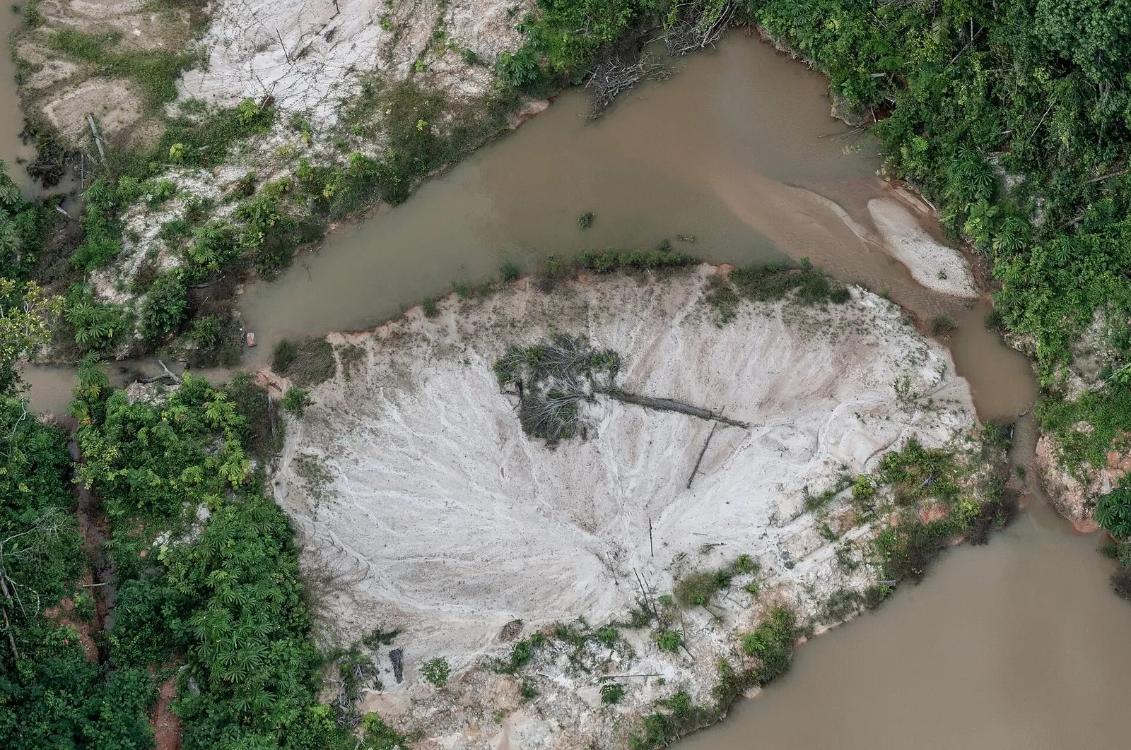 Vista aérea de uma área de garimpo na floresta, com uma grande mancha de areia clara exposta cercada por água barrenta e vegetação