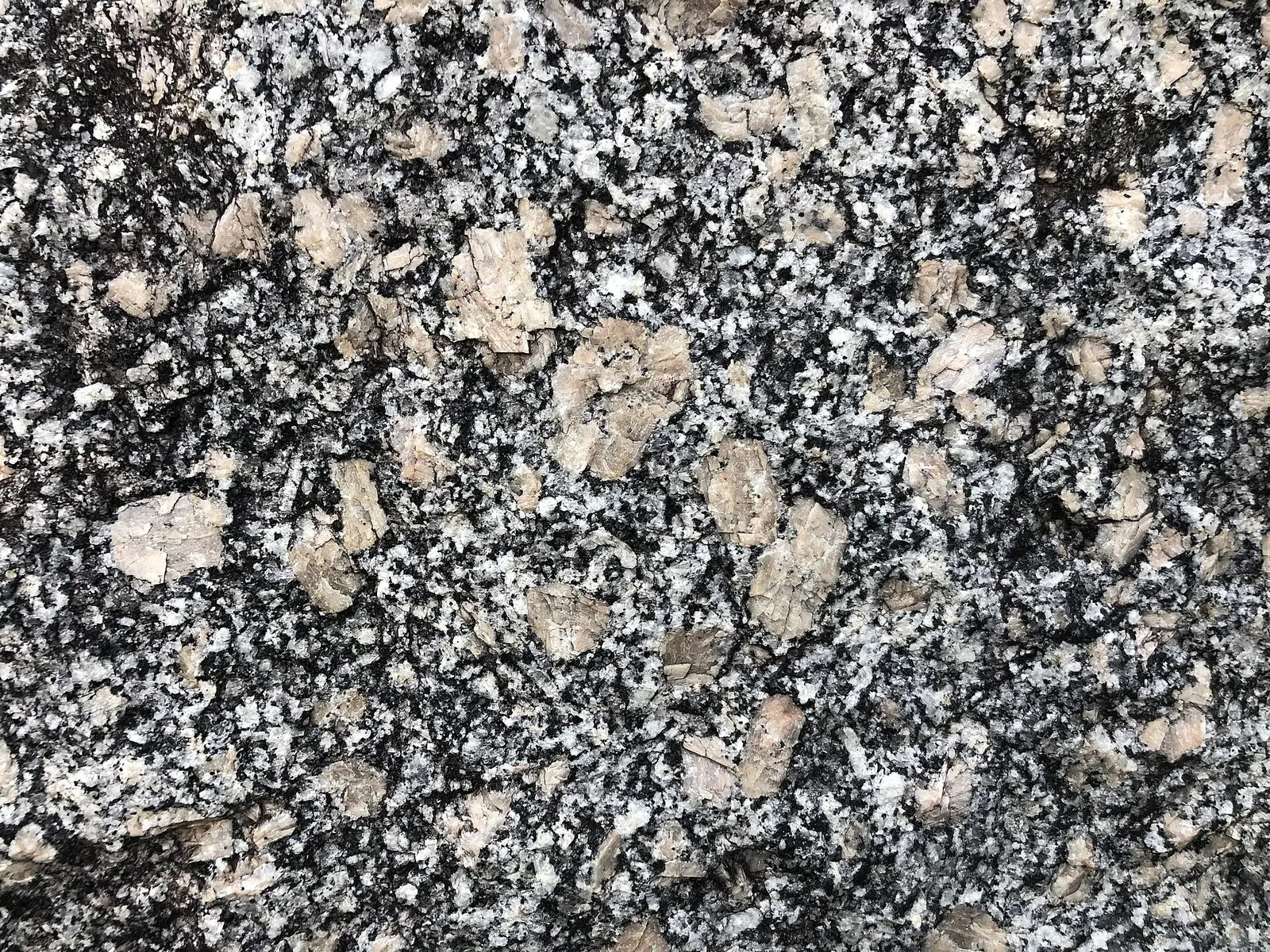 Superfície de granito com grãos claros, cinzentos e pretos misturados e cristais maiores de cor bege rosada