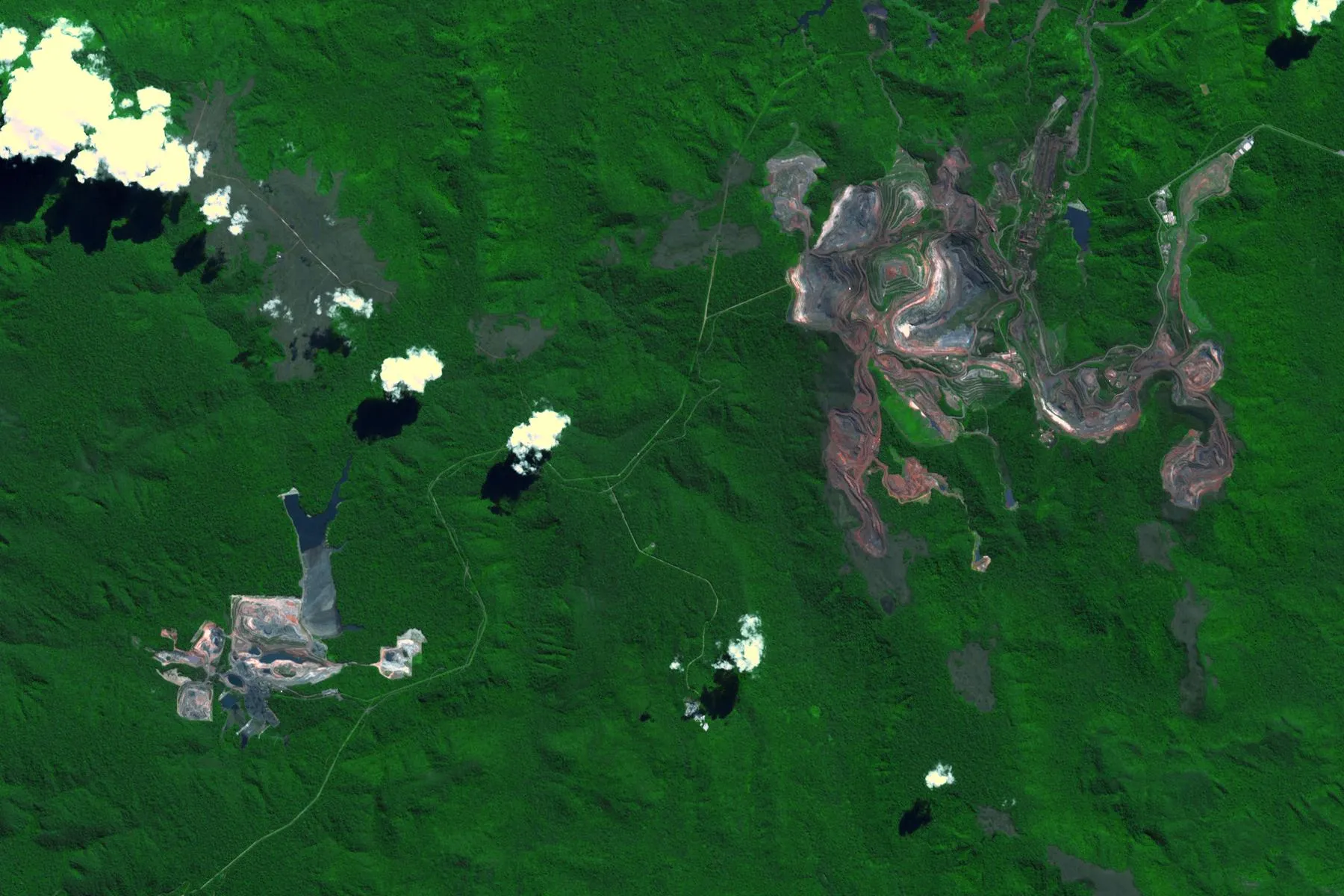 Imagem de satélite de áreas de mineração de Carajás, no Pará, cercadas por floresta, com cavas em tons de vermelho e cinza