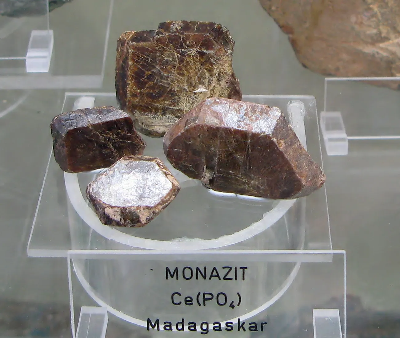Quatro cristais marrons de monazita sobre um suporte de acrílico, com etiqueta de museu