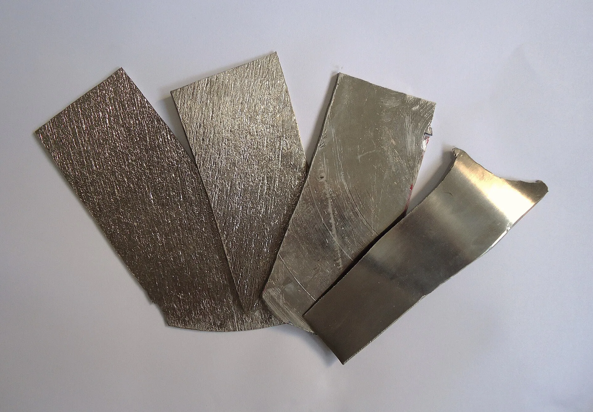Duas tiras finas de metal prateado e brilhante, uma delas com a ponta escurecida, apoiadas sobre uma superfície clara