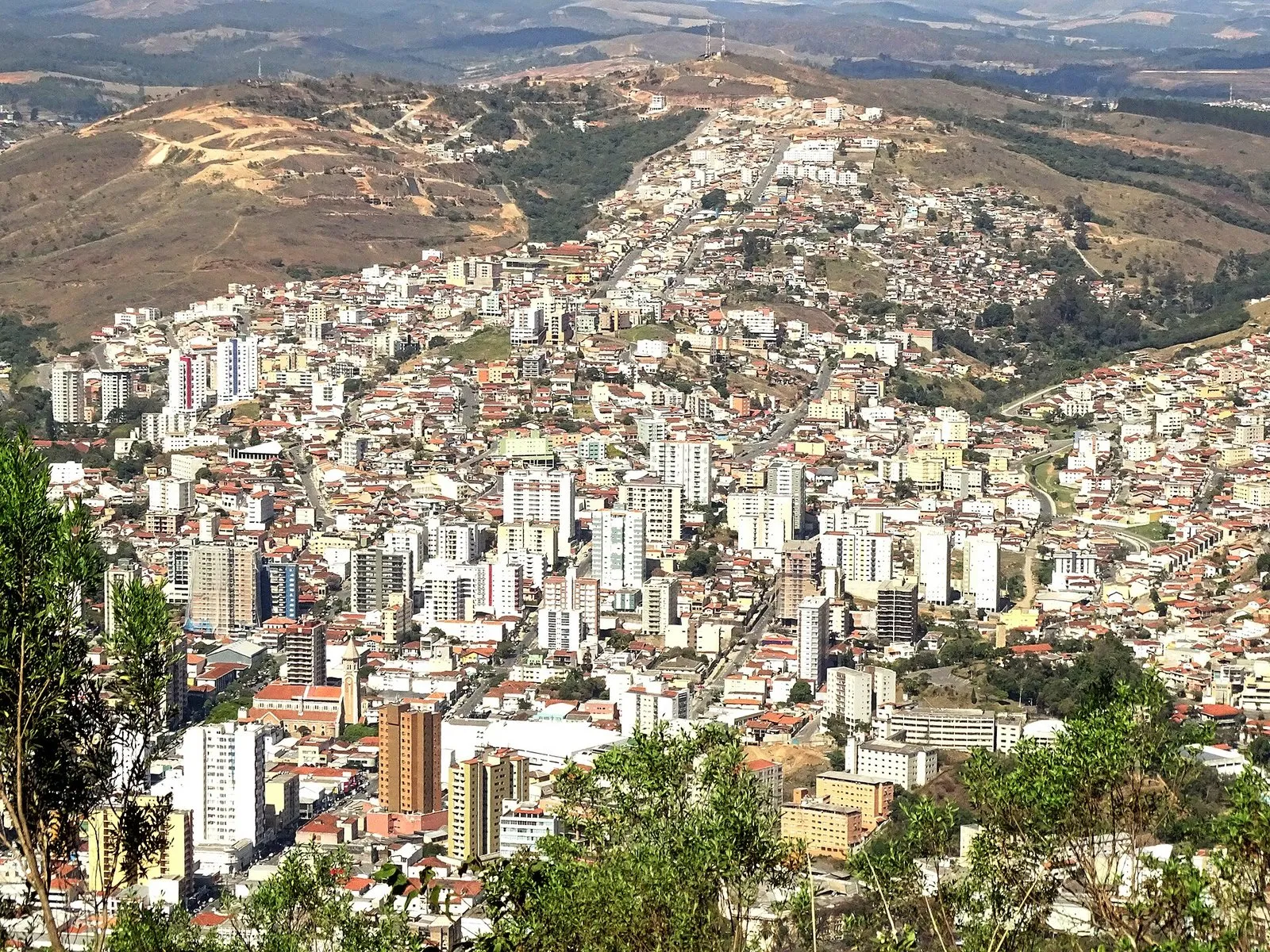 Vista do alto da cidade de Poços de Caldas, com prédios e casas no vale e morros ao fundo