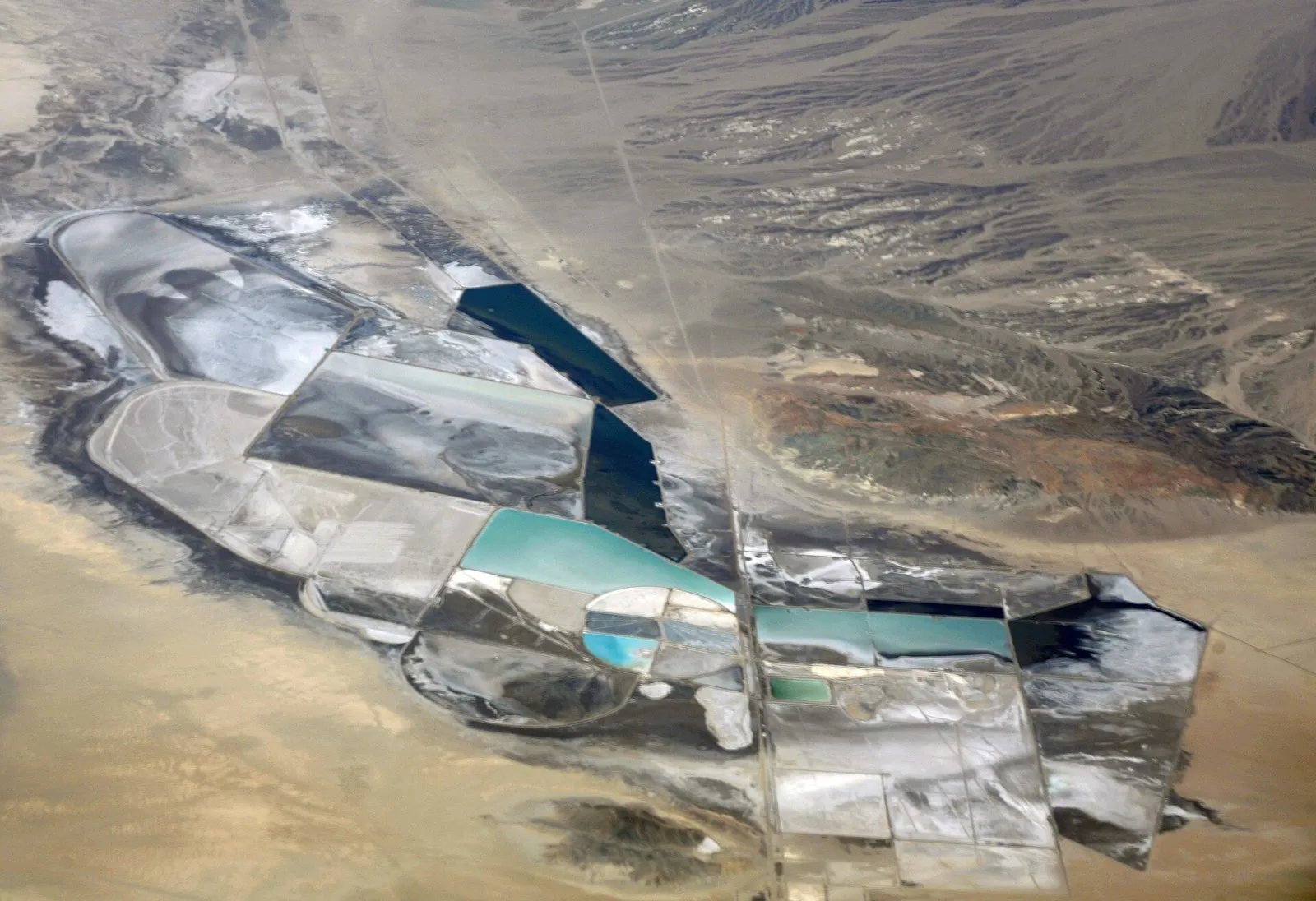 Vista aérea de um conjunto de tanques retangulares no deserto, com água em tons de azul-turquesa, azul-escuro e branco de sal